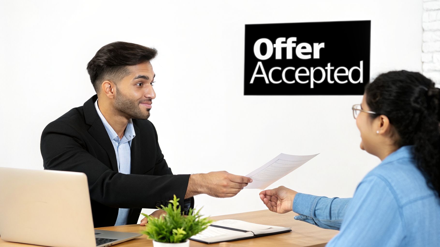 A man hands an 'Offer Accepted' document to a woman during a professional meeting.