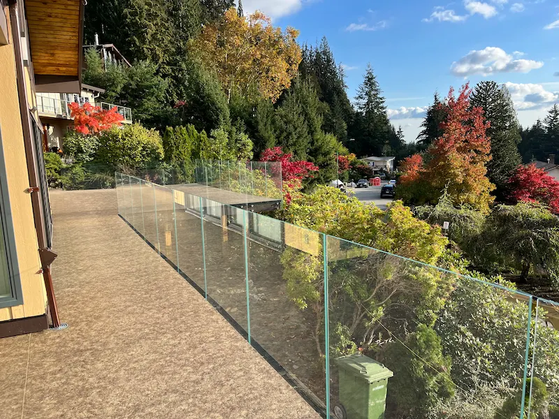 Frameless glass railing along a balcony overlooking trees and mountains, enhancing open outdoor views.