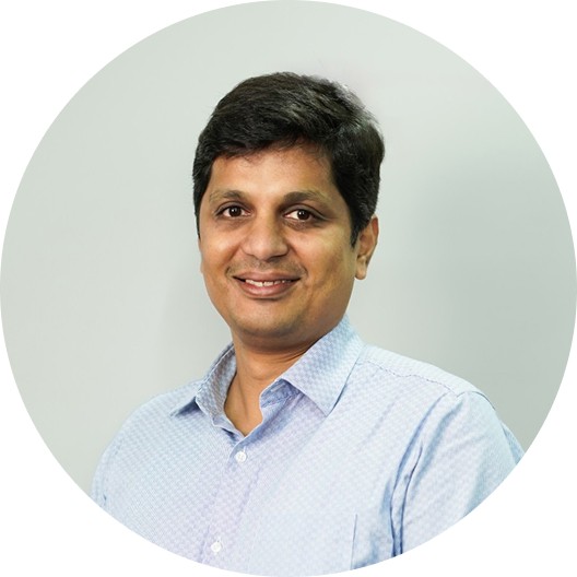 Portrait of a young man with wavy dark hair and a trimmed beard in a white sweater, soft light on a neutral background.