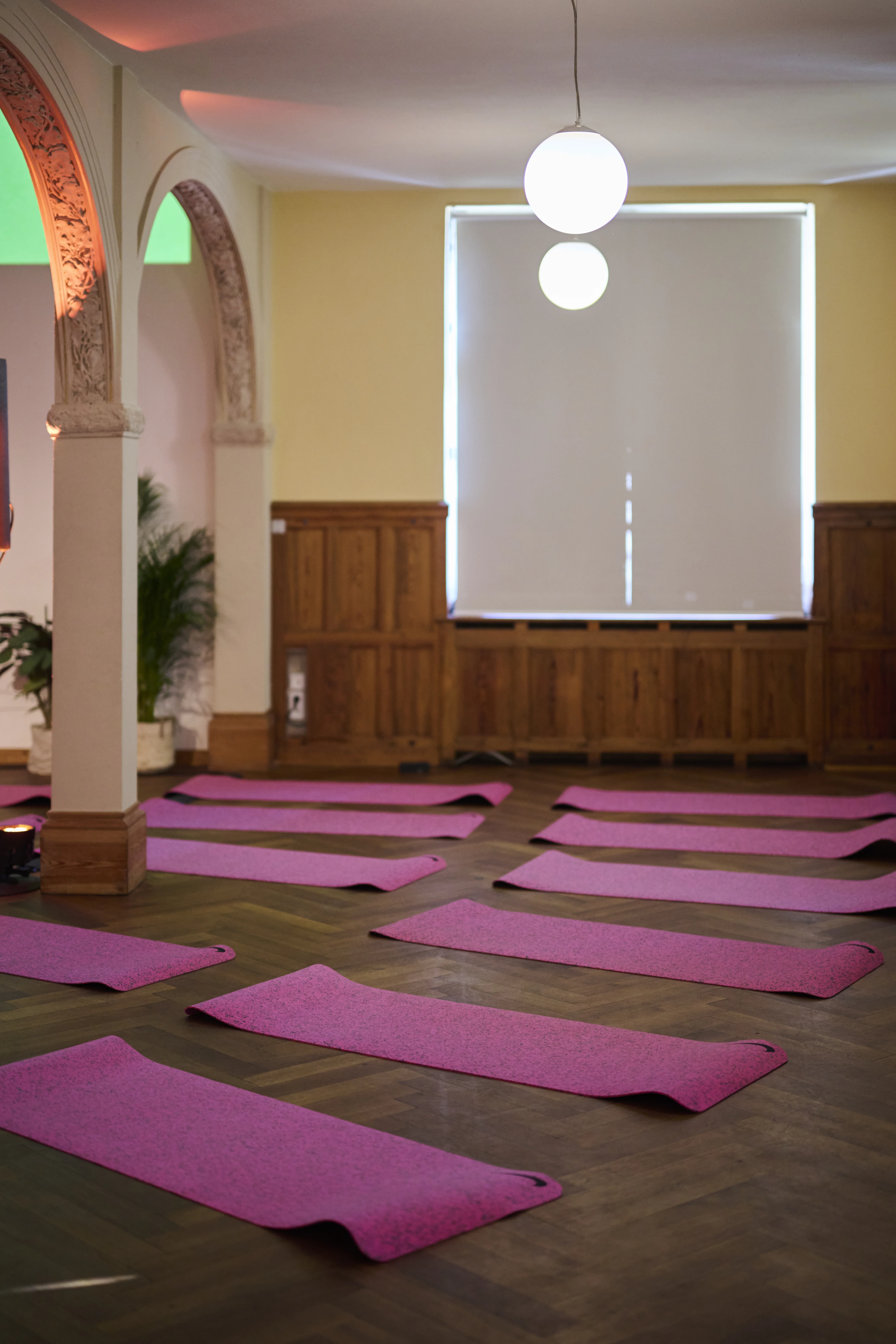 Yoga room with pink mats on parquet floor, wood panelling and globe pendant lights.