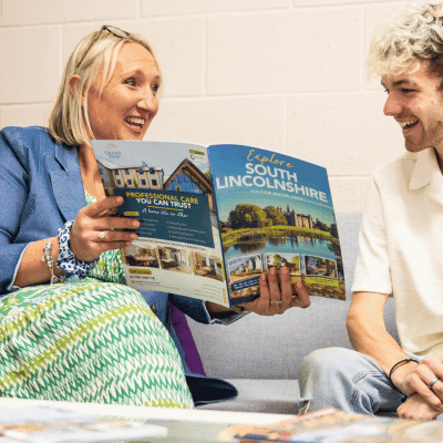 Male and female, smiling and conversating over a printed magazine.