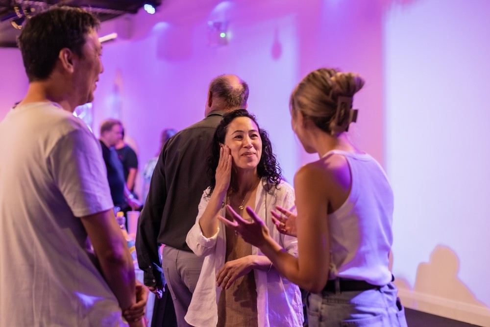A speaker on stage, illuminated against a dark background, gestures while addressing an audience.