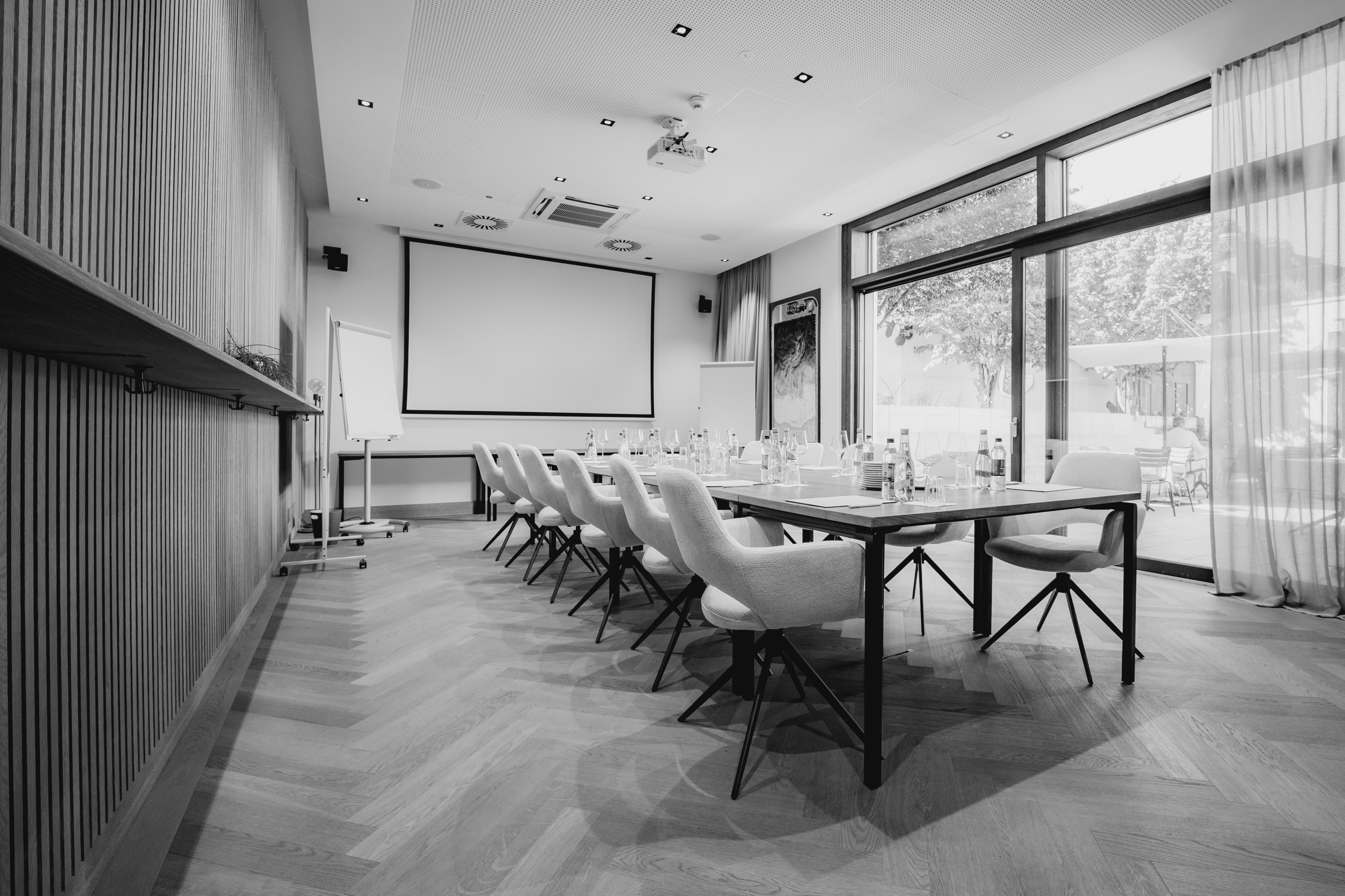 A modern classroom in black and white, featuring desks, a large screen, and windows with natural light.