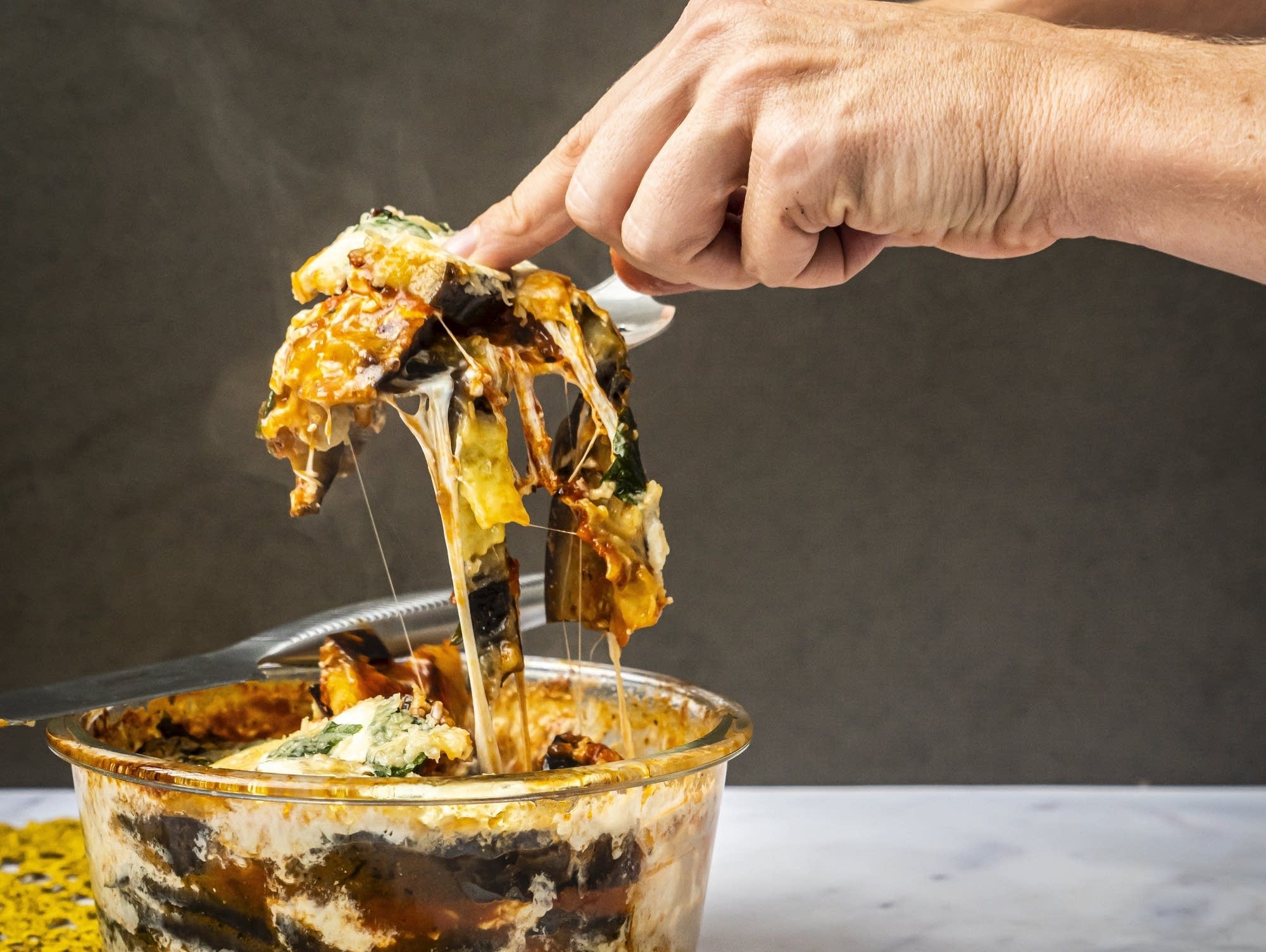 Fork lifting eggplant parmesan from a clear glass baking dish