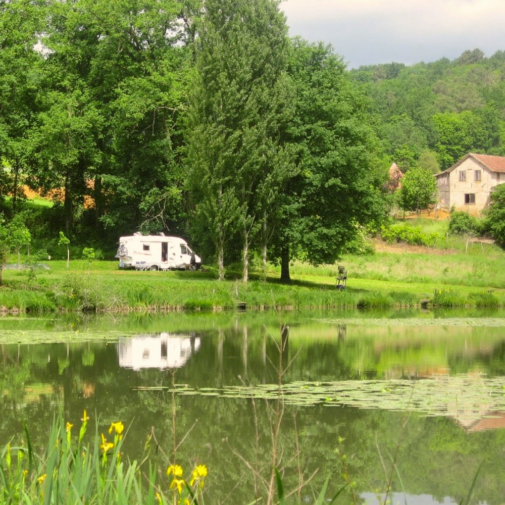 Photo prise au bord de l'eau au domaine de la brame, avec en arrière-plan de l'autre côté de l'étang un emplacement calme pour un camping car en nature