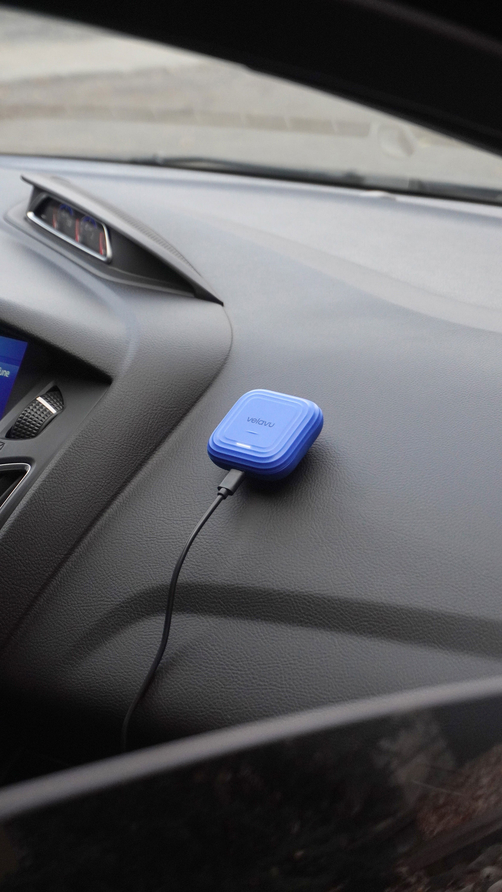 GPS tracking module clipped onto the dashboard of a car, displaying a compact, modern device with a sleek design for navigation and tracking purposes.