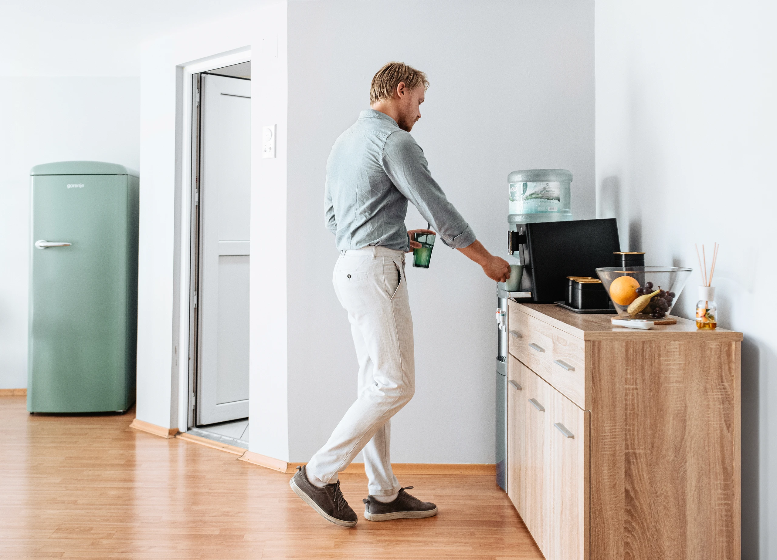 Auxality employee taking a short break at the water dispenser during a workday in a modern office.