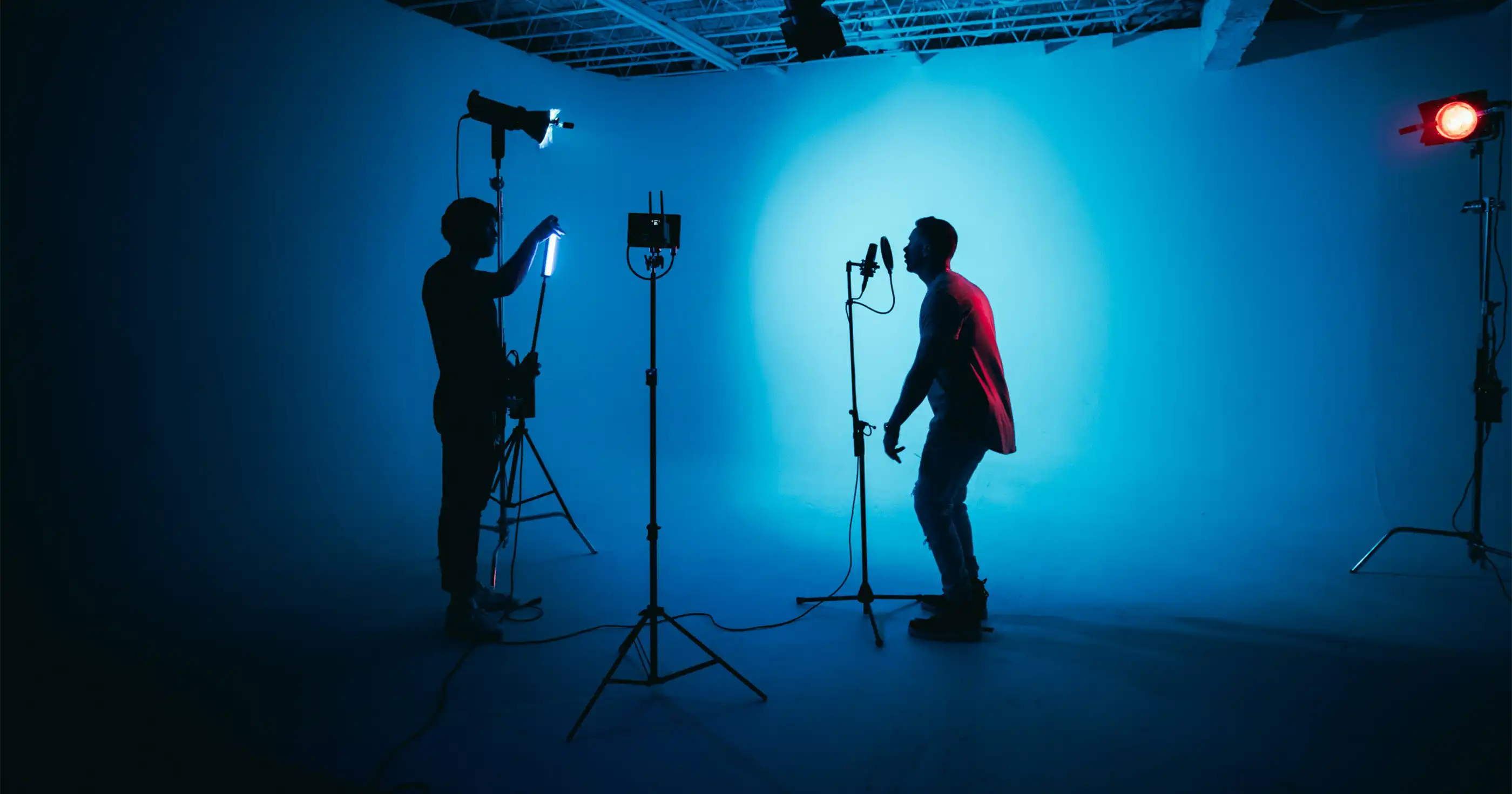 a siloette of a cameraman is shooting video of a singer against a blue background