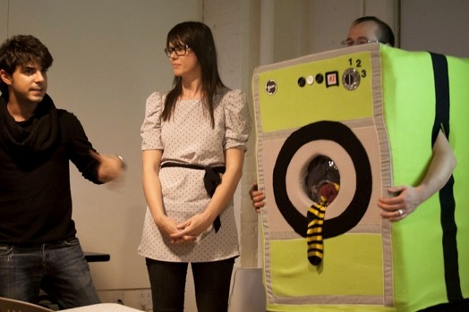 A photo of three people, one wearing a washing machine costume with socks popping from it.