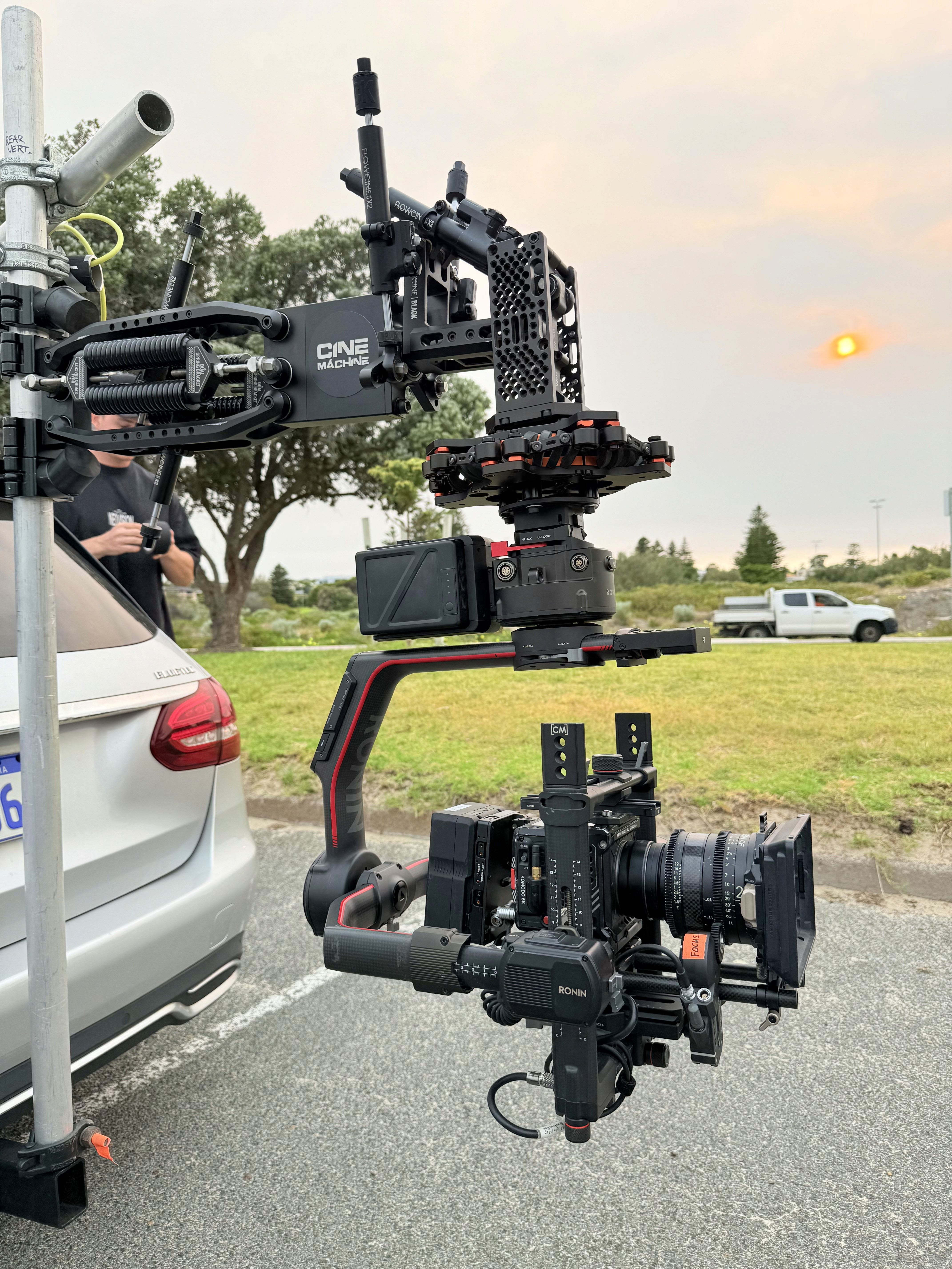 Camera on a vehicle-mounted crane arm beside a second camera on a gimbal, rigged for a tracking shot at dusk