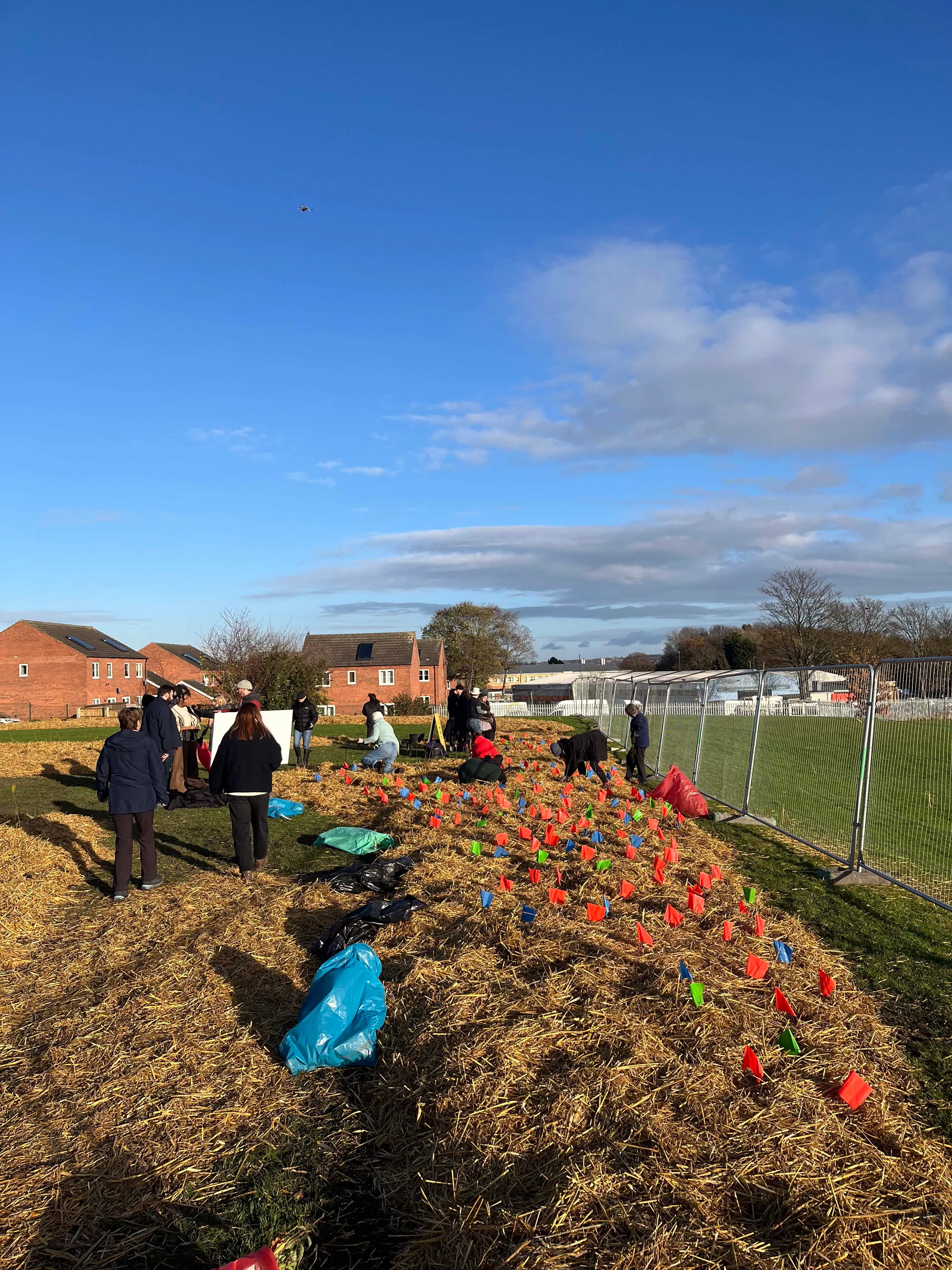 A group of people working outdoors in a garden under a blue sky, with fields visible in the background.