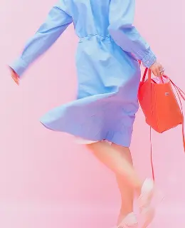 lower body parts without the head of a woman wearing a blue aproan, cream shoe and red color bag in hand