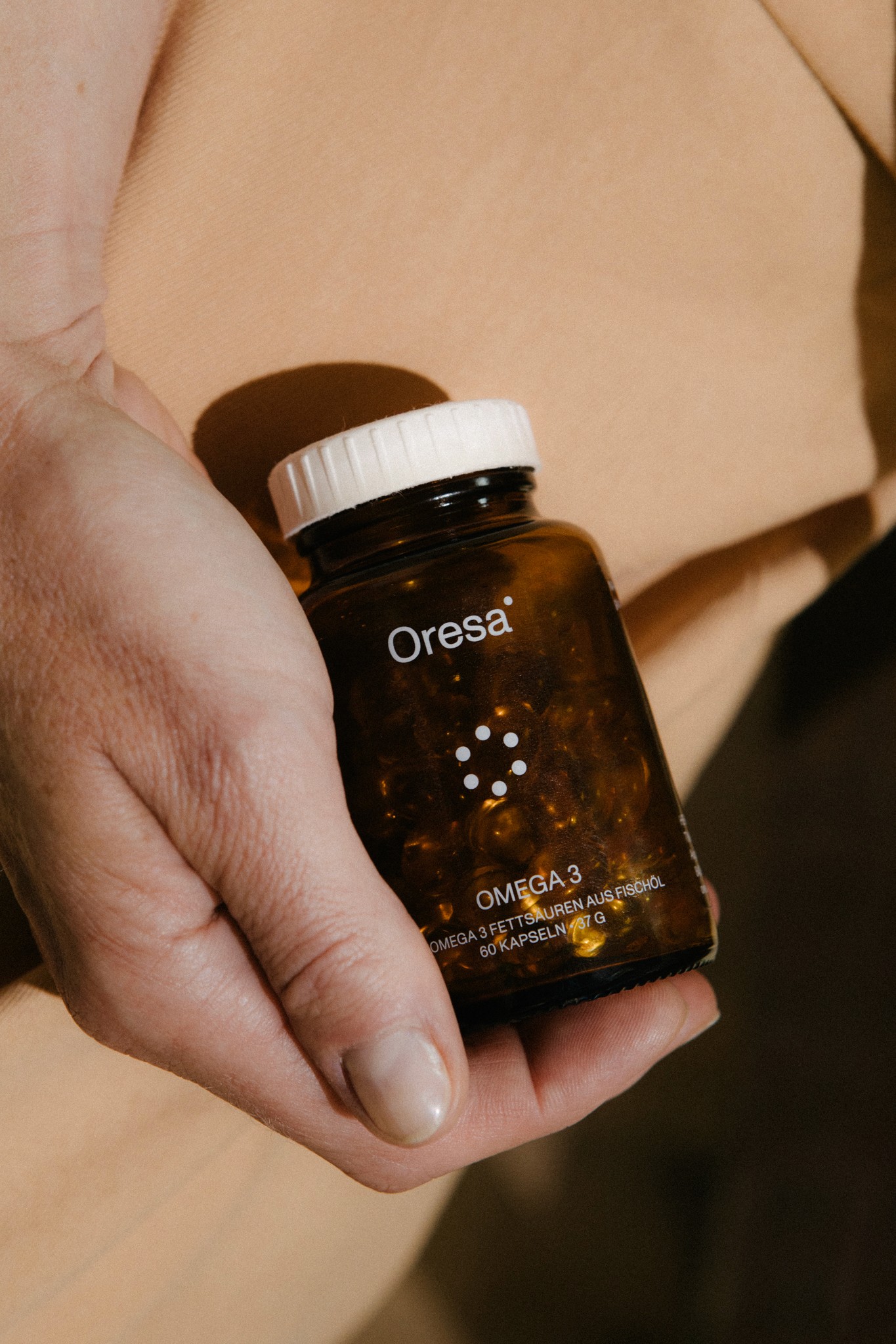 Hand hält Oresa Omega-3 Kapseln in Glasflasche