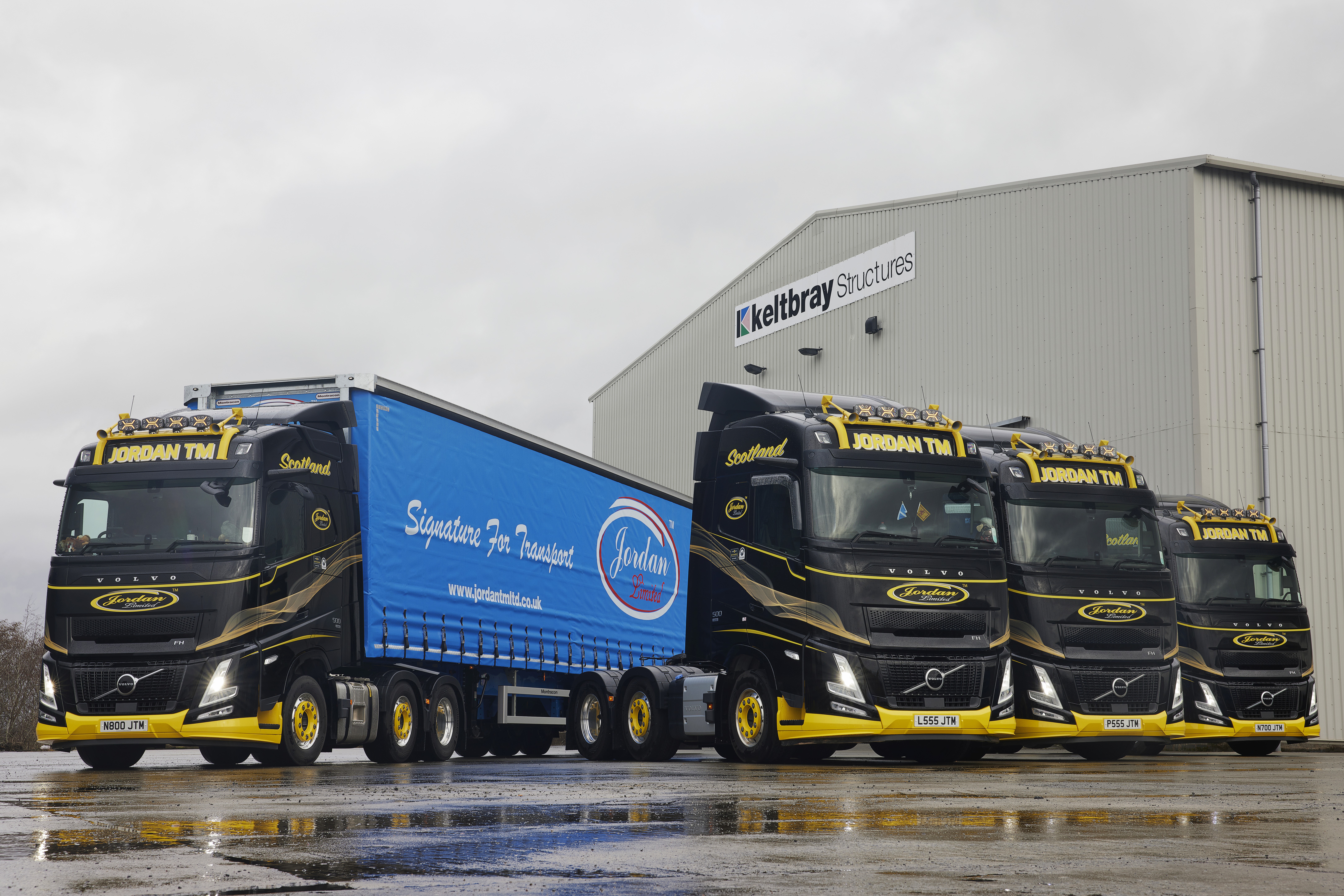 A bright blue Scania truck with "BLACKS" branding drives through an industrial area. Nearby, there are large black and white shipping containers.