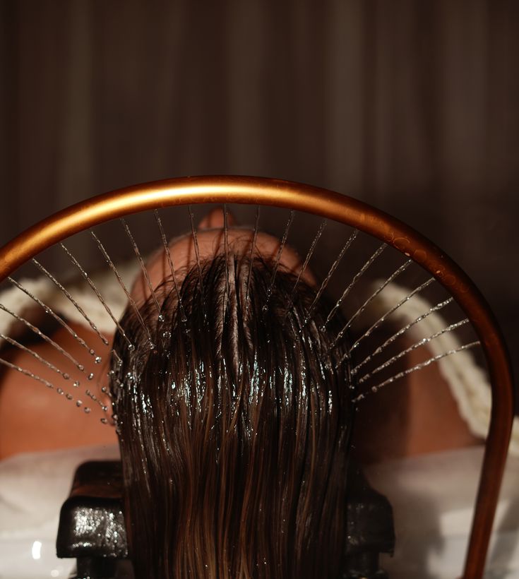 A woman with radiant skin and a white towel wrapped around her head, gazing softly at the camera. Warm sunlight filters through, casting gentle shadows on her face, enhancing the serene and fresh spa-like atmosphere.