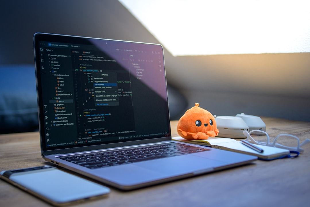 Laptop with code, phone, glasses, and plush toy.