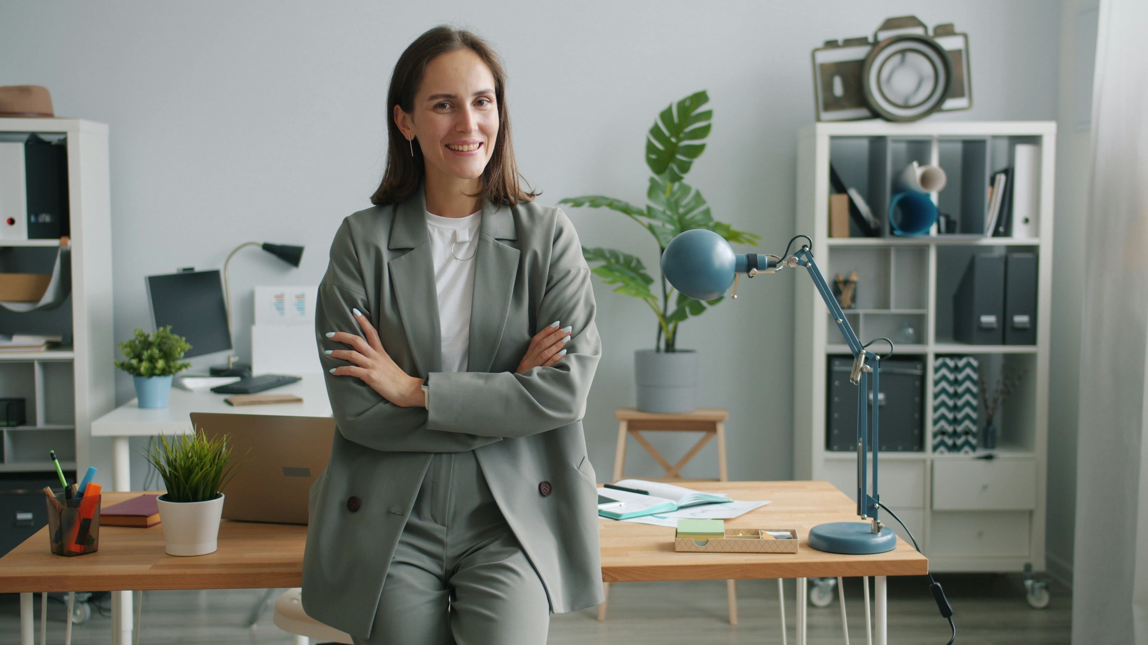 A woman in a grey suit smiles with arms crossed.