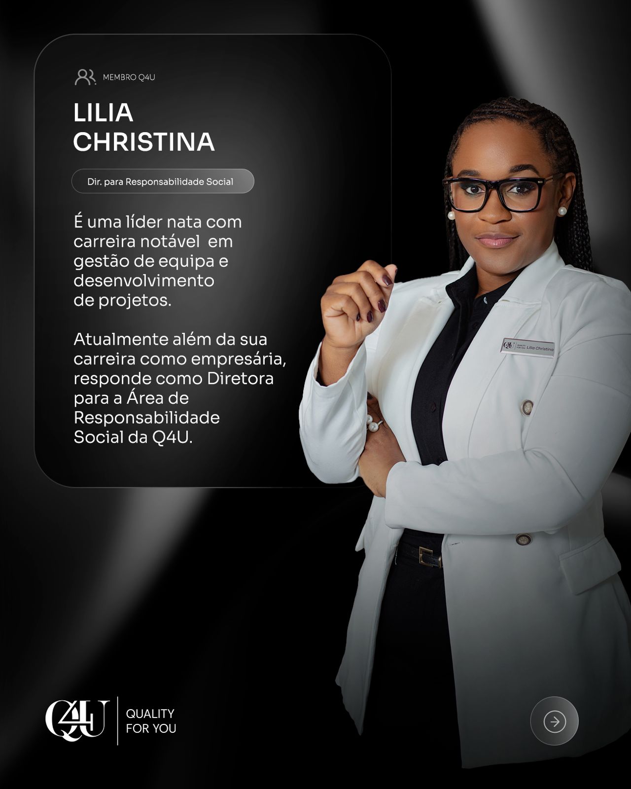 A woman with long red hair in a black sleeveless top smiles warmly. She stands in a softly lit room, conveying a cheerful and welcoming mood.