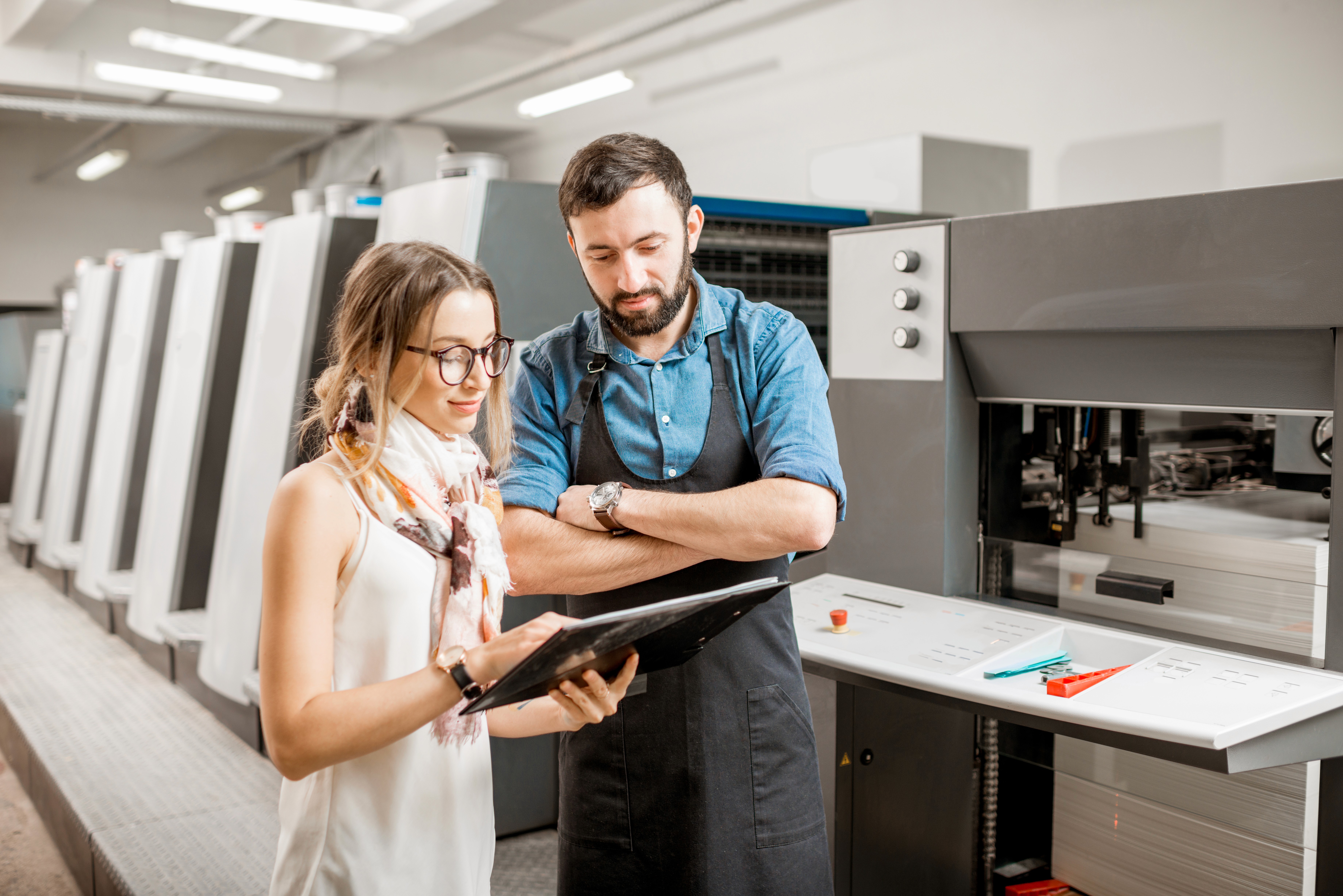 A man and woman discuss a tablet in a modern kitchen with appliances in the background.