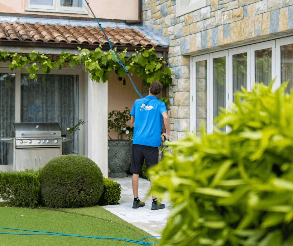 Asher using a telescopic pole system to clean upper-storey windows during an exterior clean in Whangaparāoa