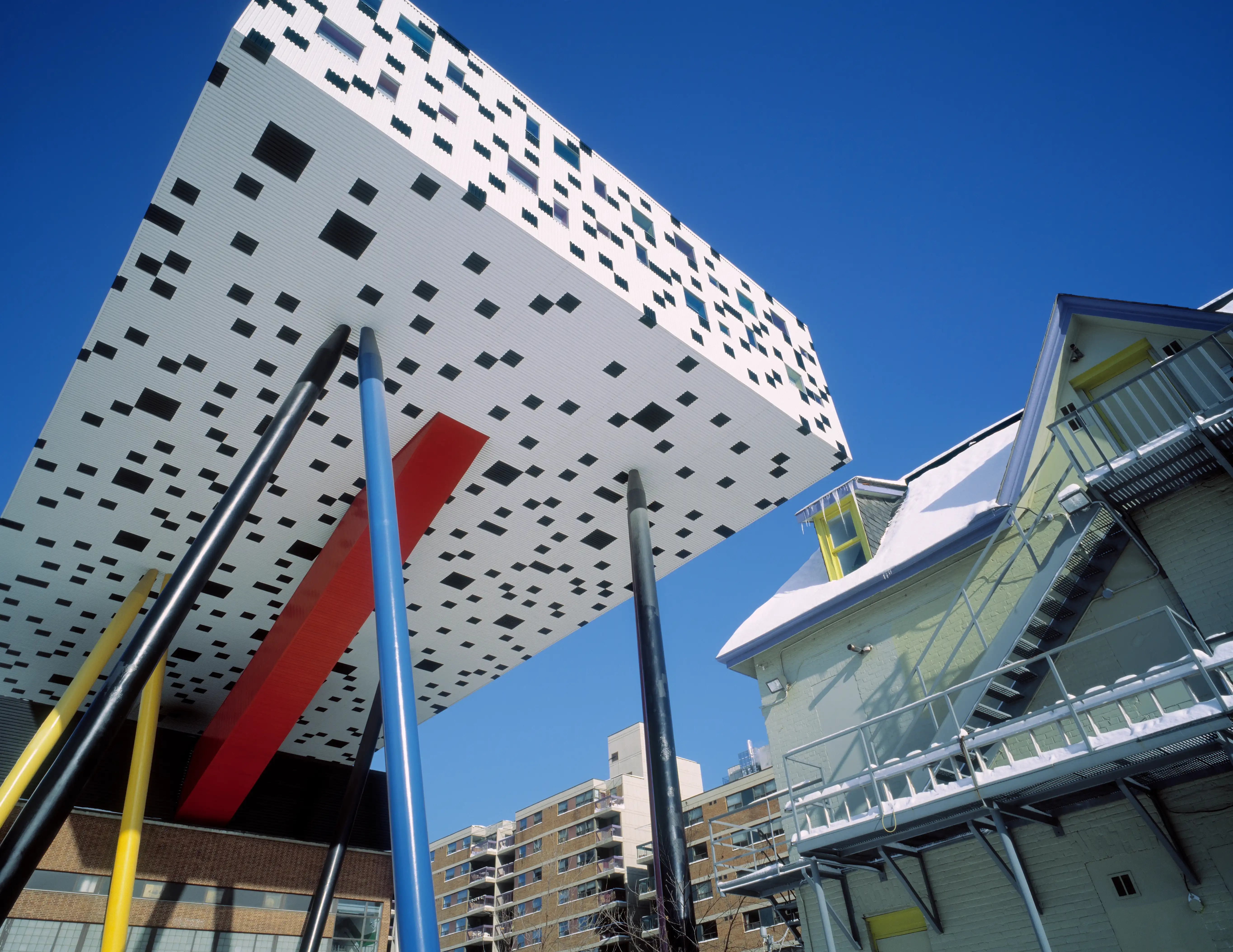 An image of OCAD University's iconic architecture: a white box with black speckles on top of an old brick building, propped by symbolic crayons.