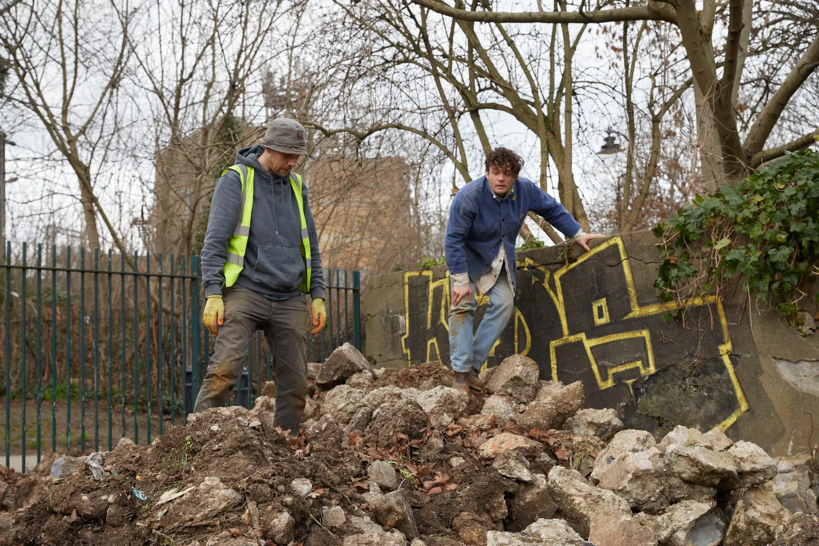 Two workers on a construction site, handling stones among trees in a natural setting.