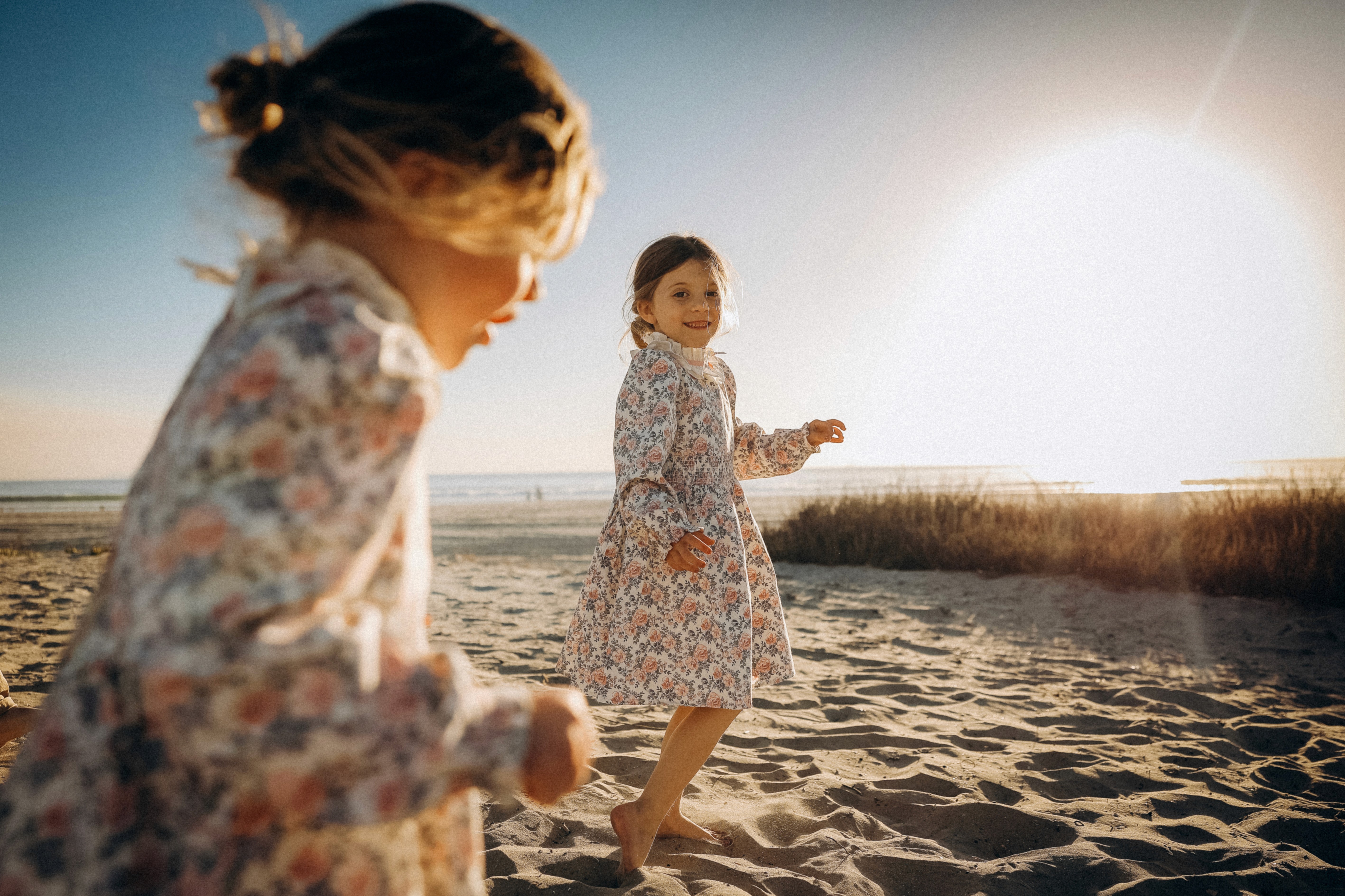 Two sisters playing on a sunlit beach during a family sunset session in San Diego