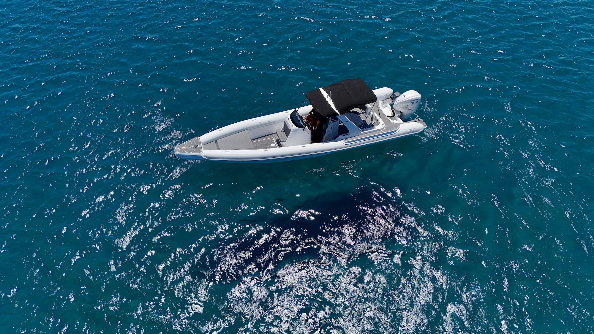 White Fost Matrix 32 speedboat with black bimini top cruising in crystal-clear turquoise waters of the Aegean Sea.