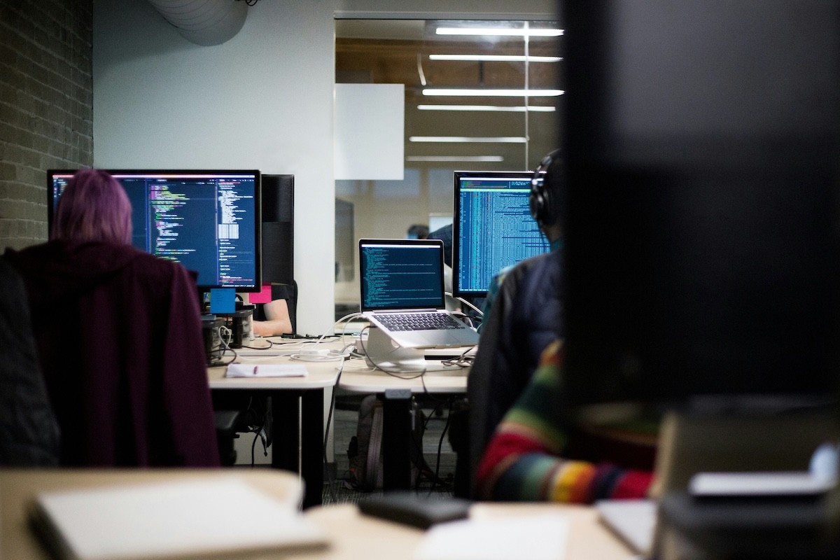 A photo of people in front of monitors programming