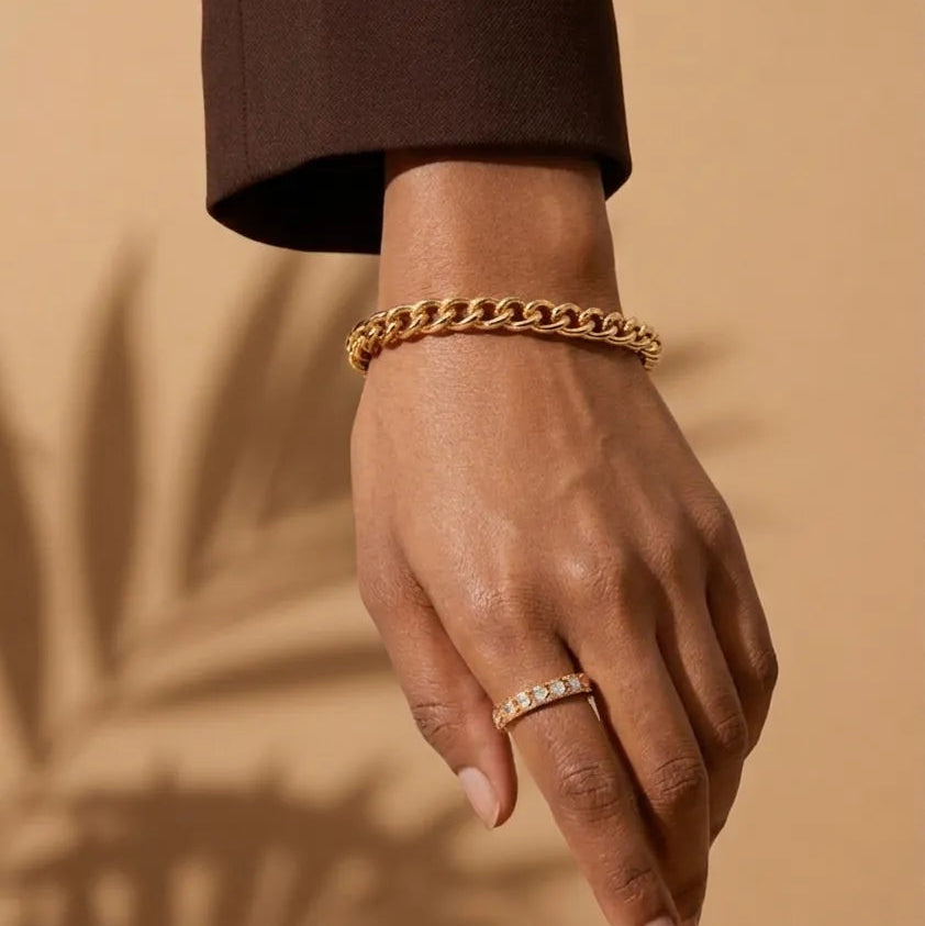 Hand wearing a gold bracelet and ring on a beige background