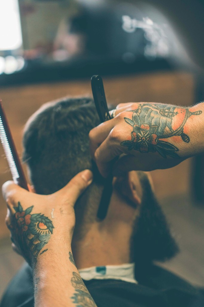 Classic Haircut in a Barbershop: A barber in a crisp white shirt gives a neat, classic haircut to a male client seated in a traditional red barber chair. The shop is well-kept with classic barber tools on display.