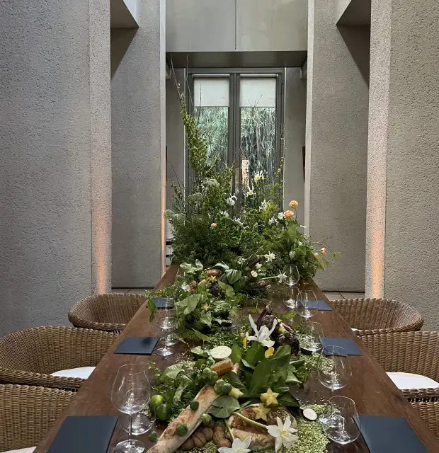 Montaje de mesa larga con centro de mesa vegetal y flores naturales para ambientación gastronómica elegante y orgánica.