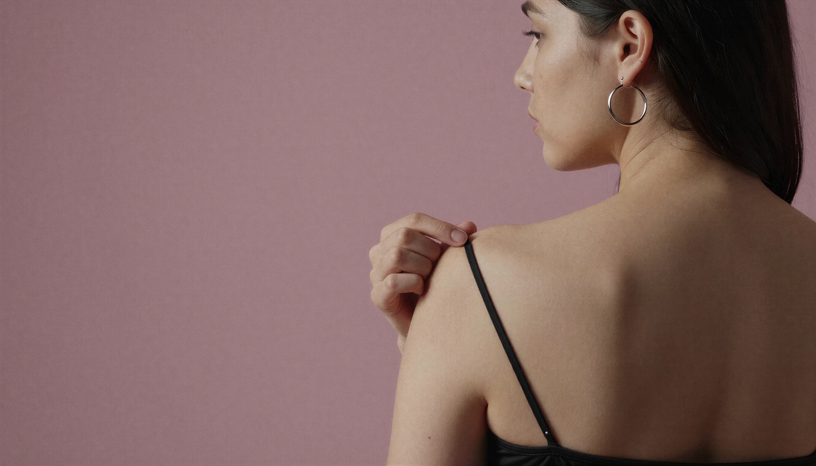 Woman adjusting a black lingerie strap in profile.