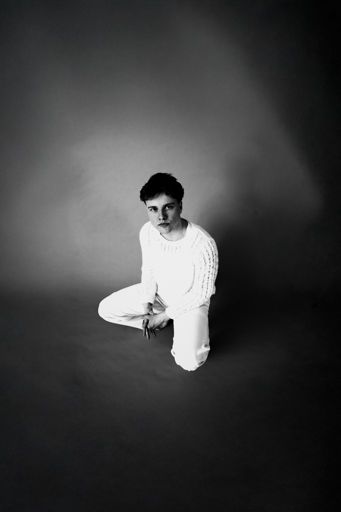 Young blonde tattooed man kneeling on the floor looking directly at the camera