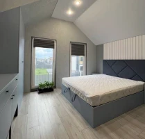 Smiling woman with natural curly hair wearing a green shirt on a solid teal background.