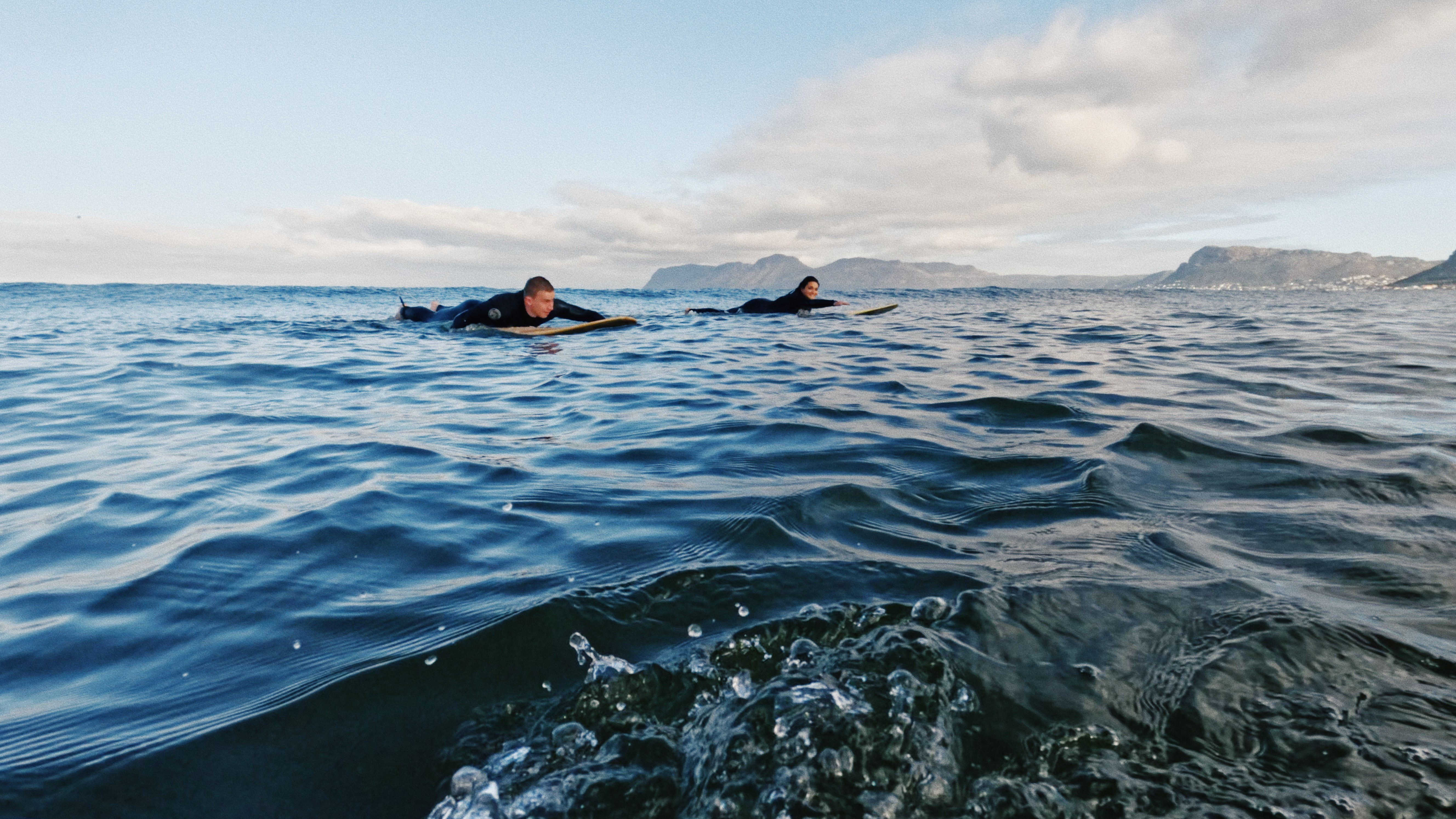 Two surf students during their surf lesson paddeling on their surfboards in Muizenberg, Cape Town