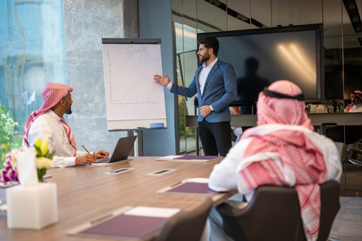 three men sitting while using laptops and watching man beside whiteboard