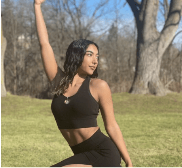 Smiling woman in beige linen outfit standing indoors with plants and books in the background.