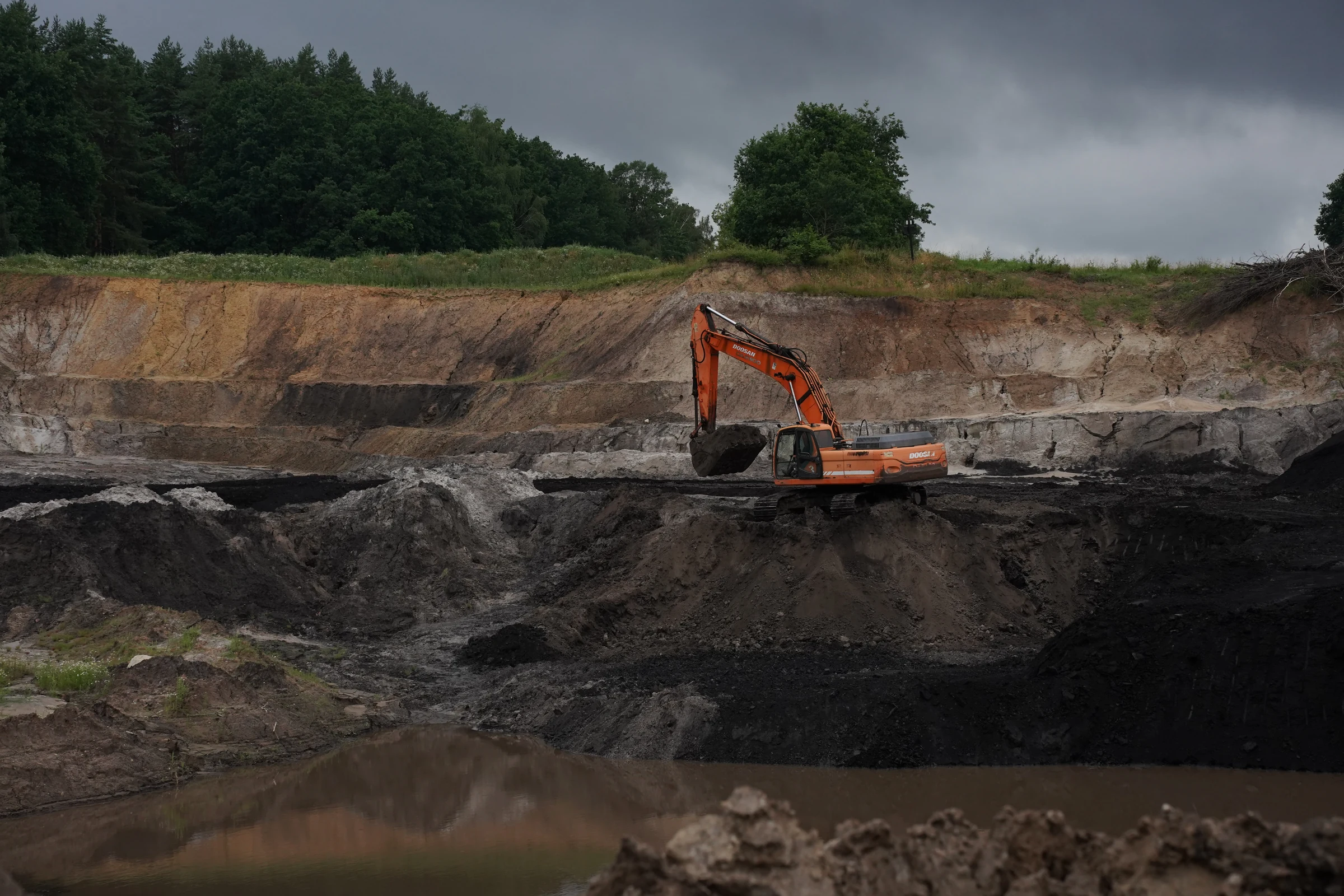 Excavator working the leonardite deposit in Poland under a stormy sky