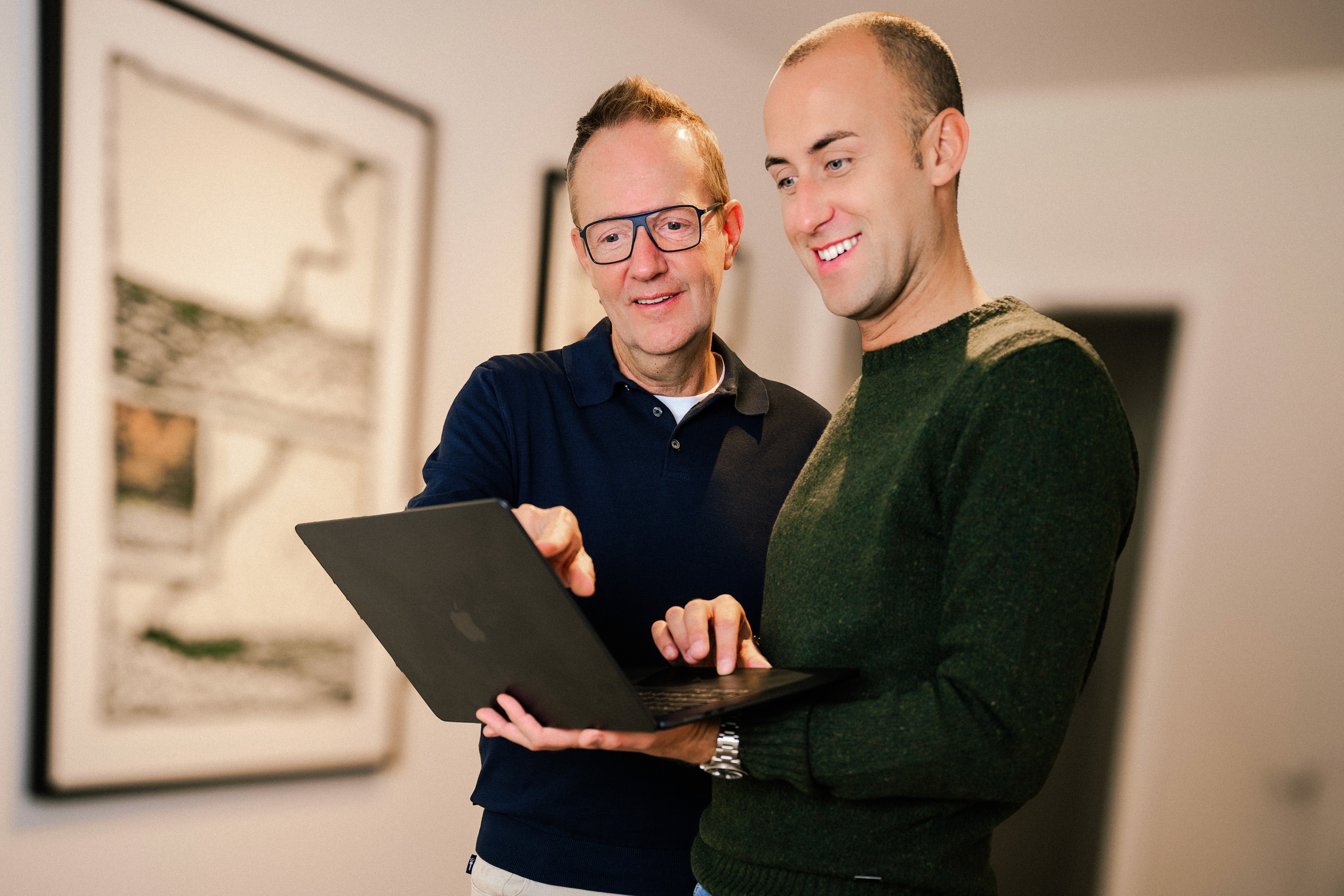 Hans en Johan staand kijkend naar laptop op arm van Johan