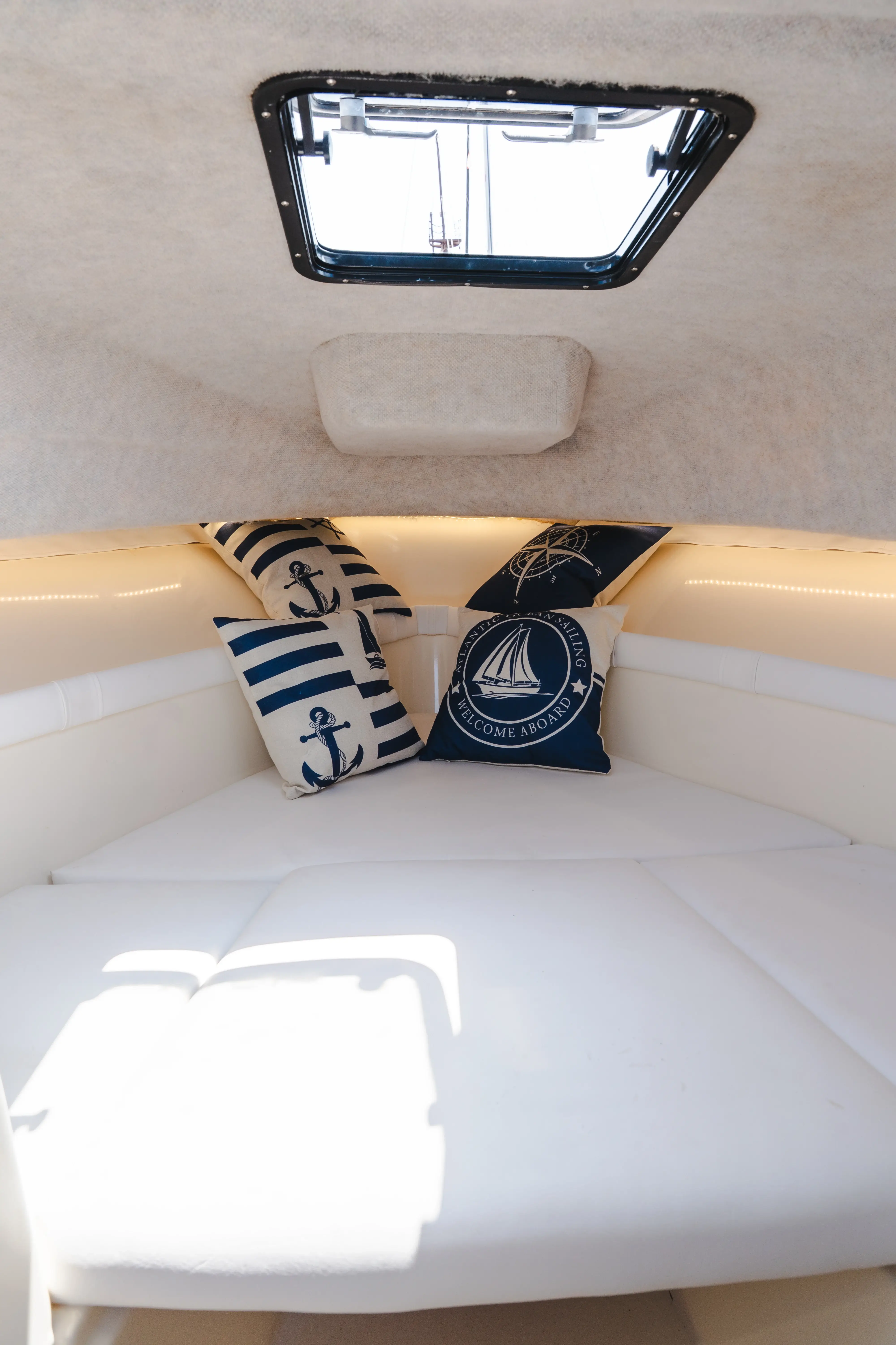 Cozy boat cabin interior with white cushioned seating and nautical decorative pillows featuring anchor and sailboat designs.
