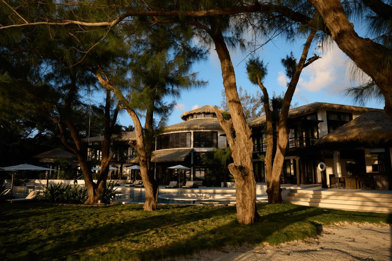 Villa Abrazos at dusk, warm lights glowing through tropical trees on the beachfront grounds.
