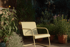 A simple white chair sits among lush green plants in a cozy outdoor space, inviting relaxation.