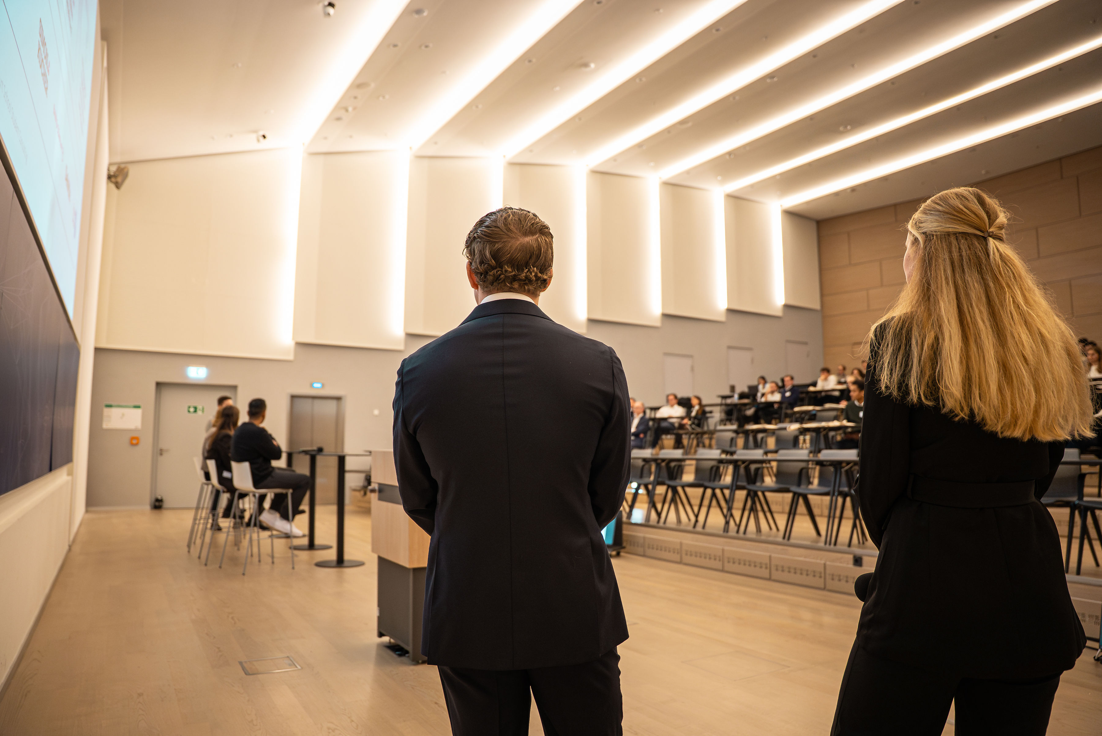 person discussing while standing in front of a large screen in front of people inside dim-lighted room