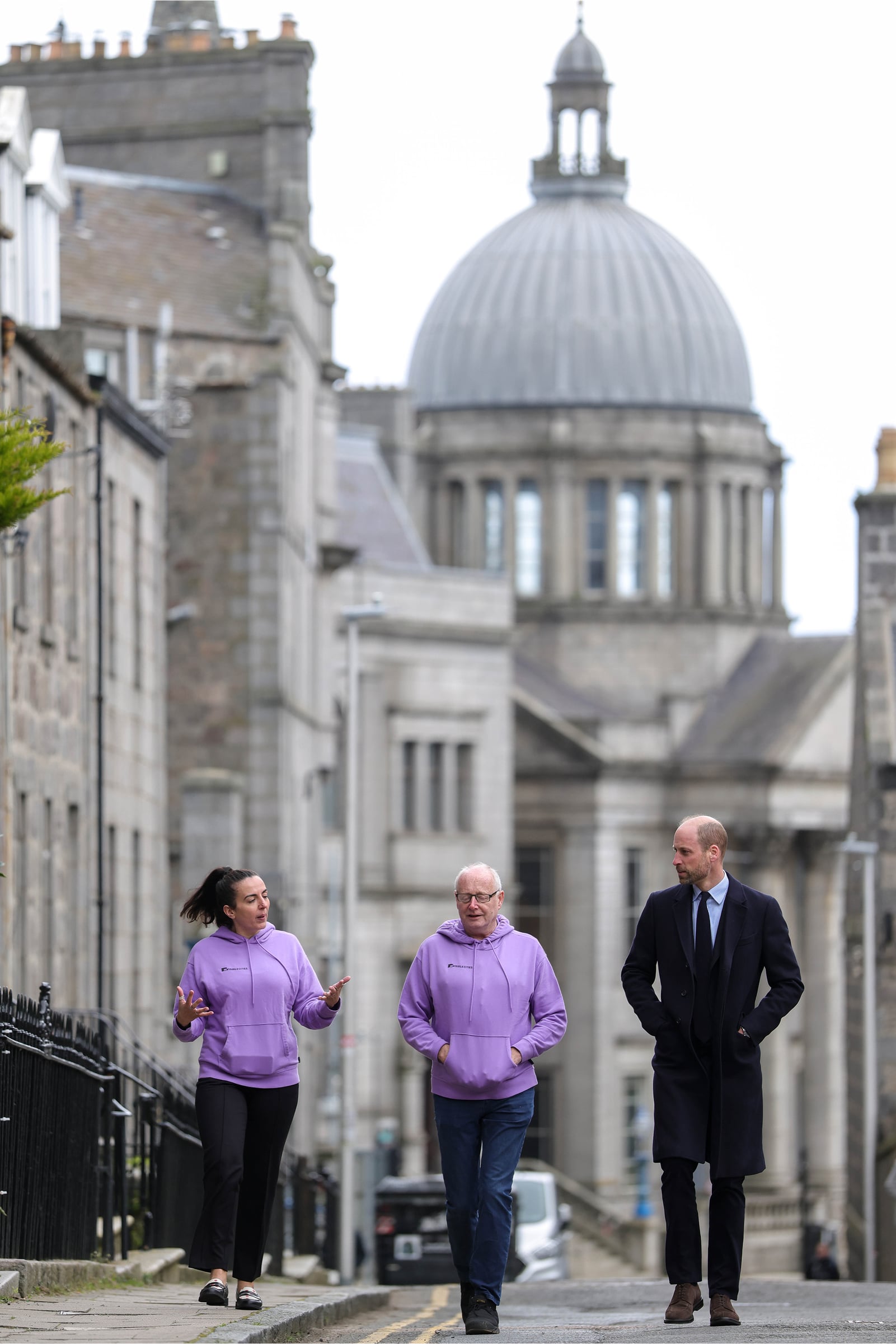 A long-distance photograph of Prince William walking down a street in Aberdeen with tour guides from Invisible Cities