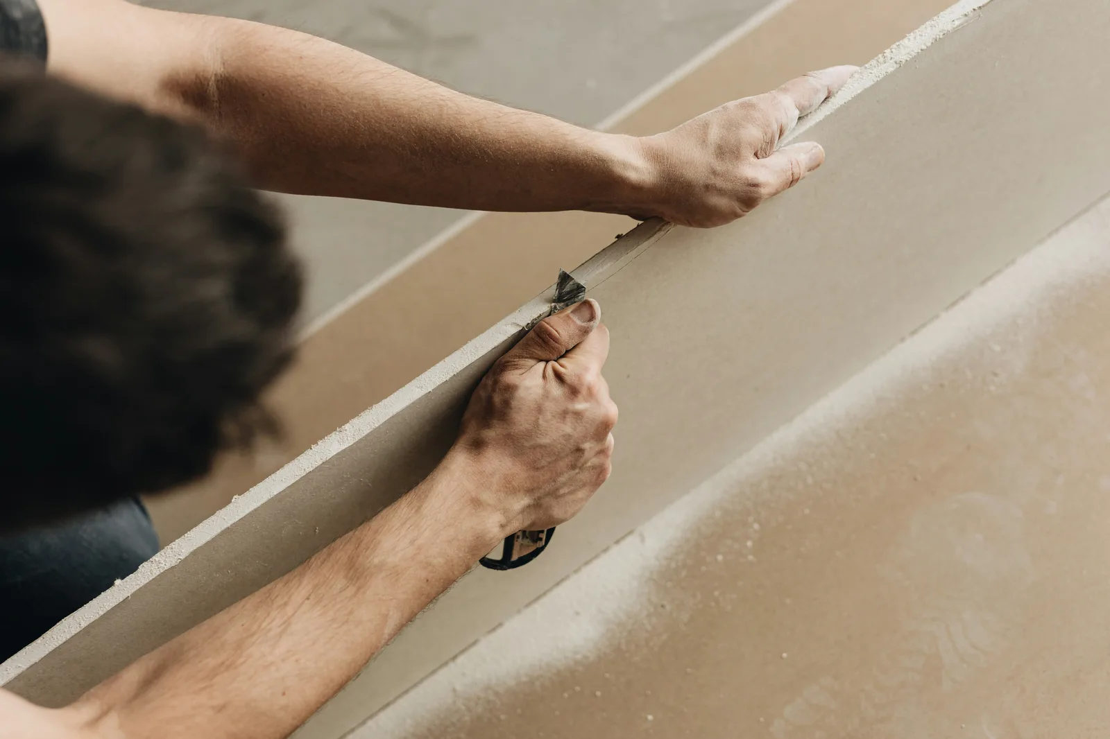 Worker cutting drywall panel with knife from overhead angle