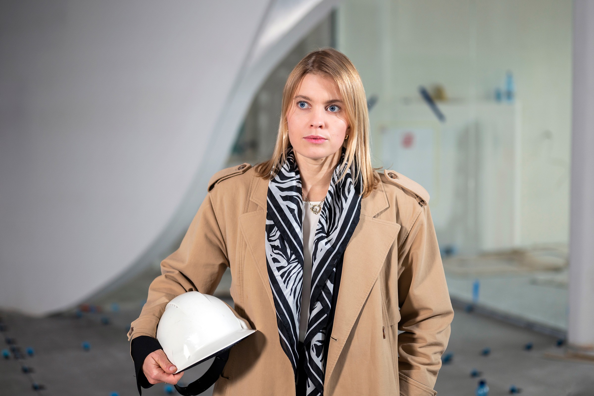 młoda kobieta, blondyka w jasnym płaszczu z białym kaskiem w ręce