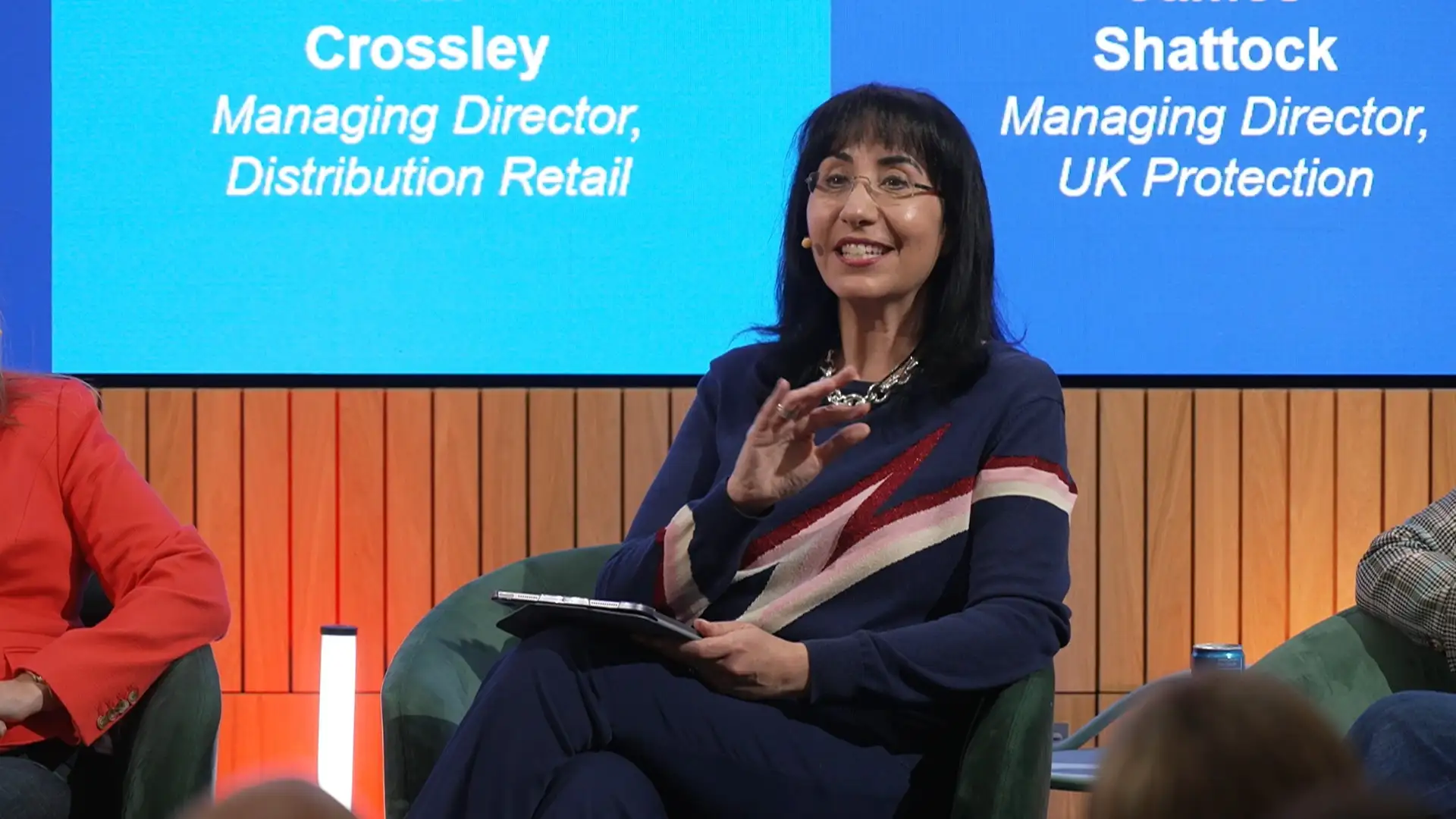 Event guest speaking on stage at the L&G Retail Tech Summit, holding notes during a live session.