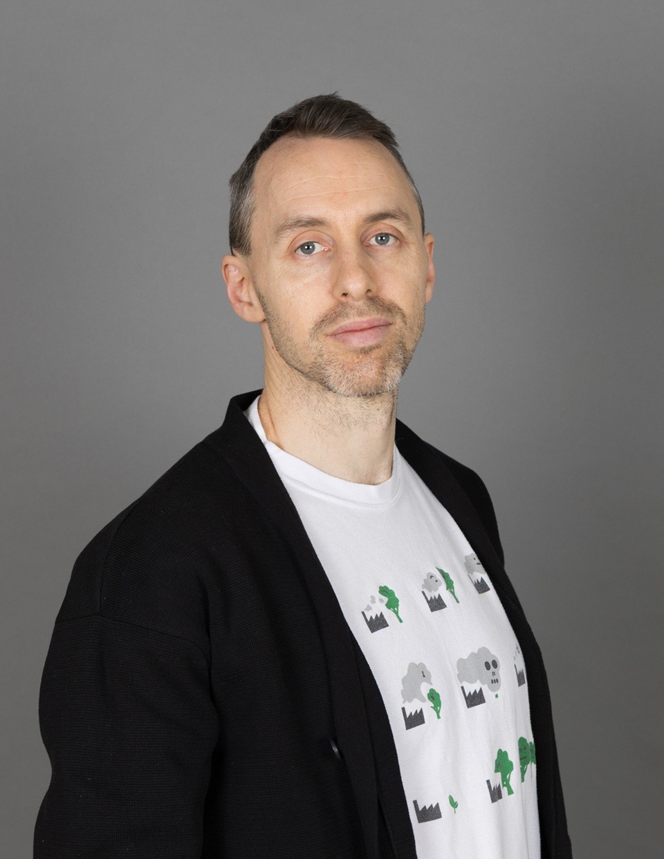 Portrait of Sandro Tagliavini founder and sole owner of Blite.ch. Portrait was taken in a studio with a dark grey background and Sandro wears a black jacket and a white t-shirt and looks into the camera.