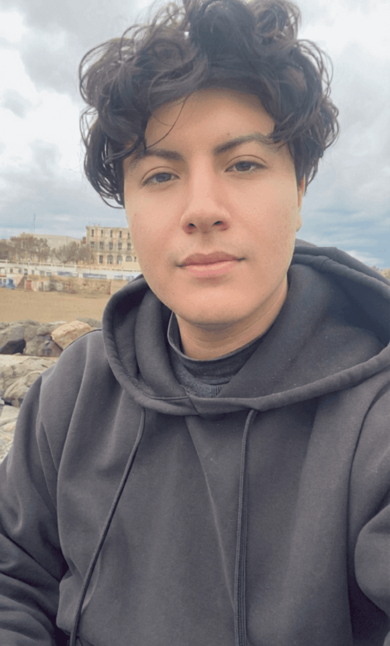 A woman with long dark hair with red highlights and glasses, posing against a simple reddish background.